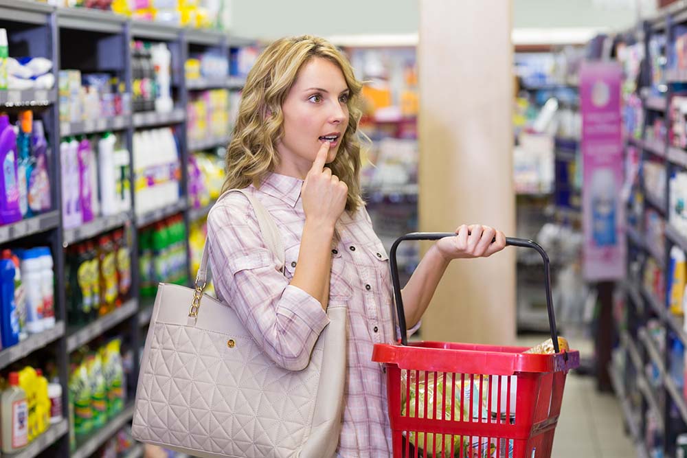 Kobieta z torbą na zakupy, patrząca w zamyśleniu na półkę w supermarkecie