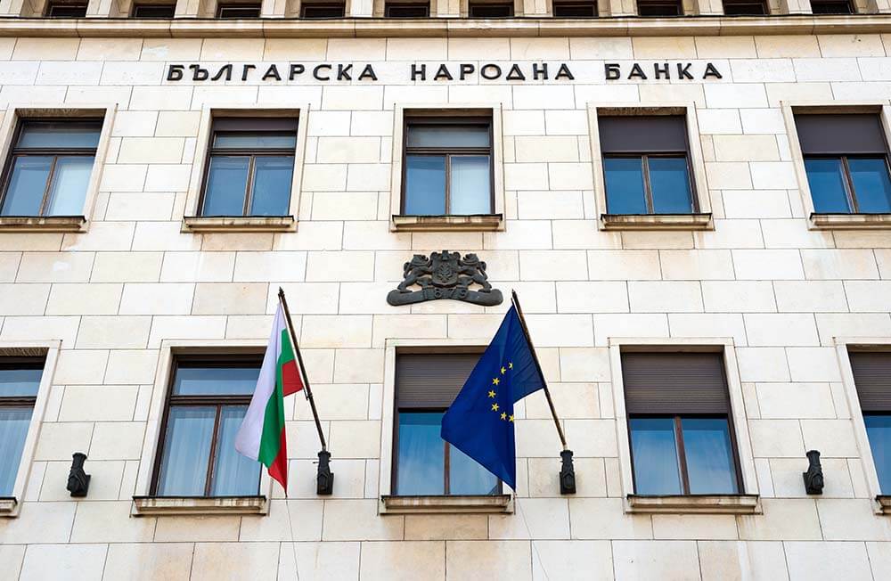 Nowoczesny budynek bułgarskiego banku z klasyczną fasadą, kolumnami i symetryczną architekturą pod czystym, błękitnym niebem